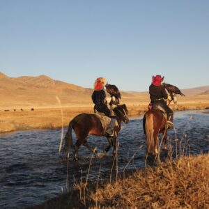 Picture of two horseriders in a river surrounded by a deserted valley with hills on the background