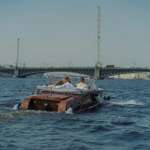 Couple enjoying a speedboat ride on a scenic river with a bridge view.